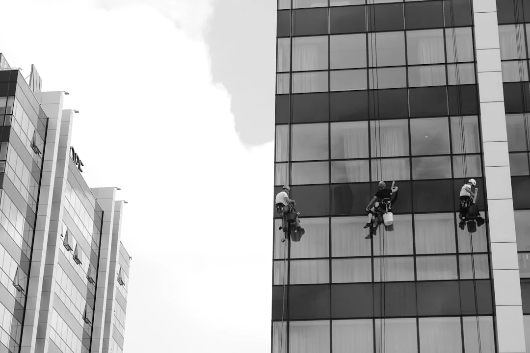 A man cleaning skyscraper windows while wearing a harness, illustrating work on urban high-rise buildings.